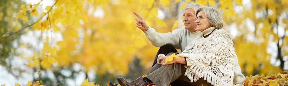 An older couple sits outdoors looking at autumn leaves, discussing a survivorship life policy.