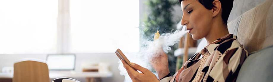 A woman using her mobile phone while smoking a vape.