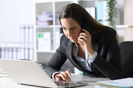 Businesswomen observing her laptop screen while concerned on a phone call.