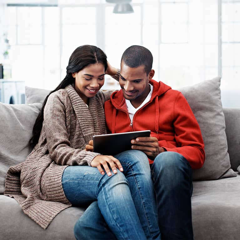 couple on the couch reviewing their finances on an ipad
