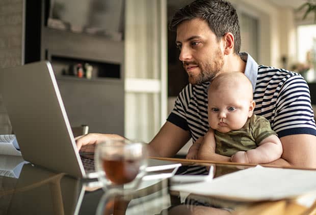 father holding his son while on the computer