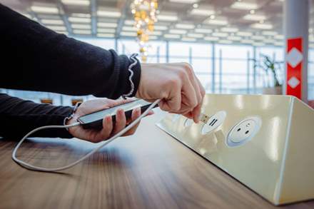 Person at the charging station of an airport, plugging in their phone.