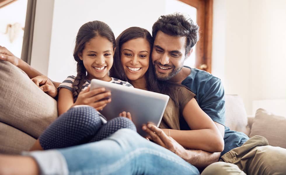 Family of three sharing a tablet on the couch