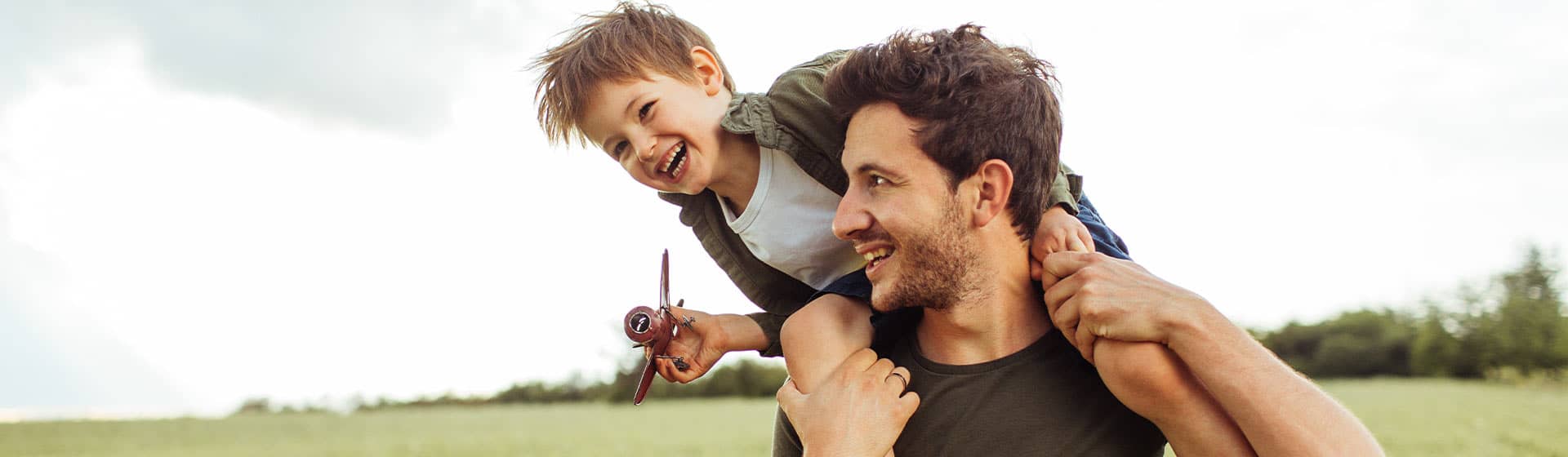 father son playing airplane in a field thinking about financial goals