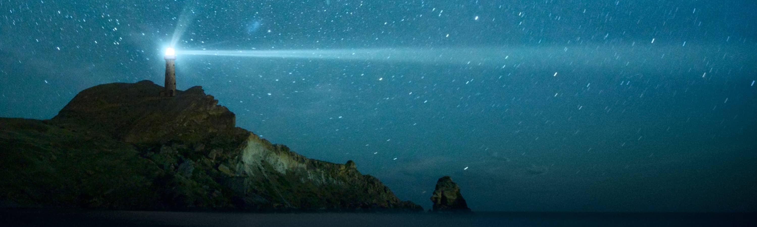 lighthouse with beacon under night sky