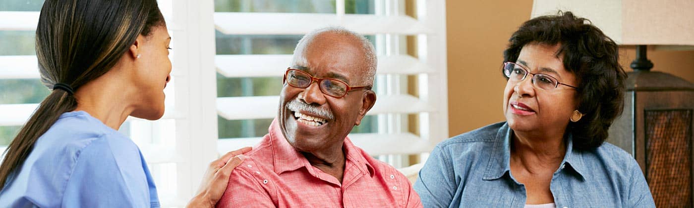 A caregiver speaks with a mature couple in their home: assisted living costs