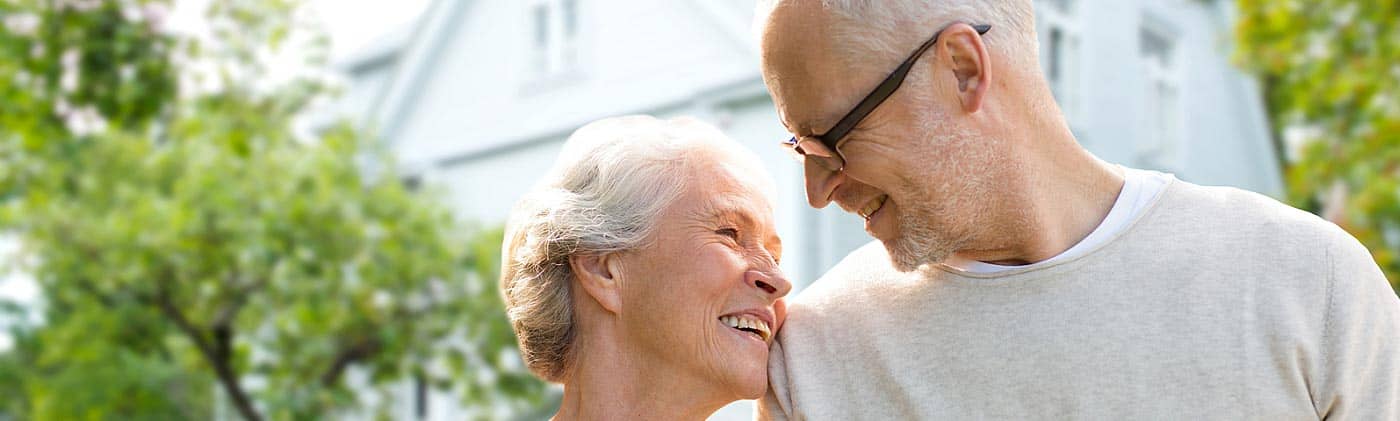 a couple smiles on a street in front of their home plan for retirement