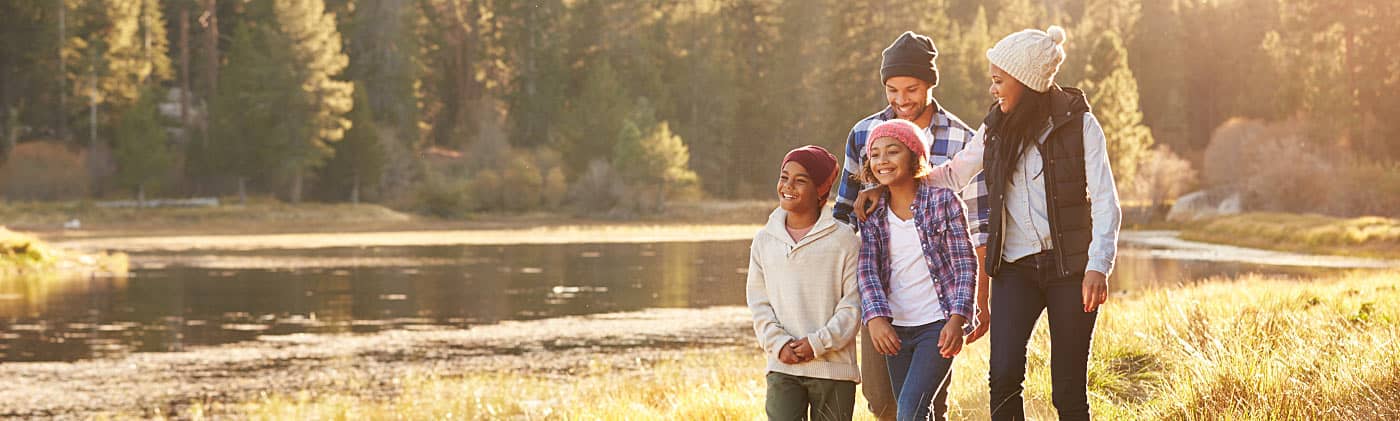 A family of four discusses the advantages of life insurance while on a sunny hike 