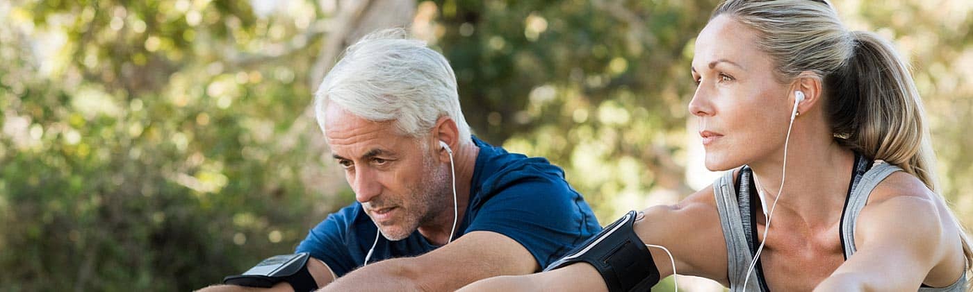 fit senior couple listens to music with earbuds and stretches before a run as part of staying healthy