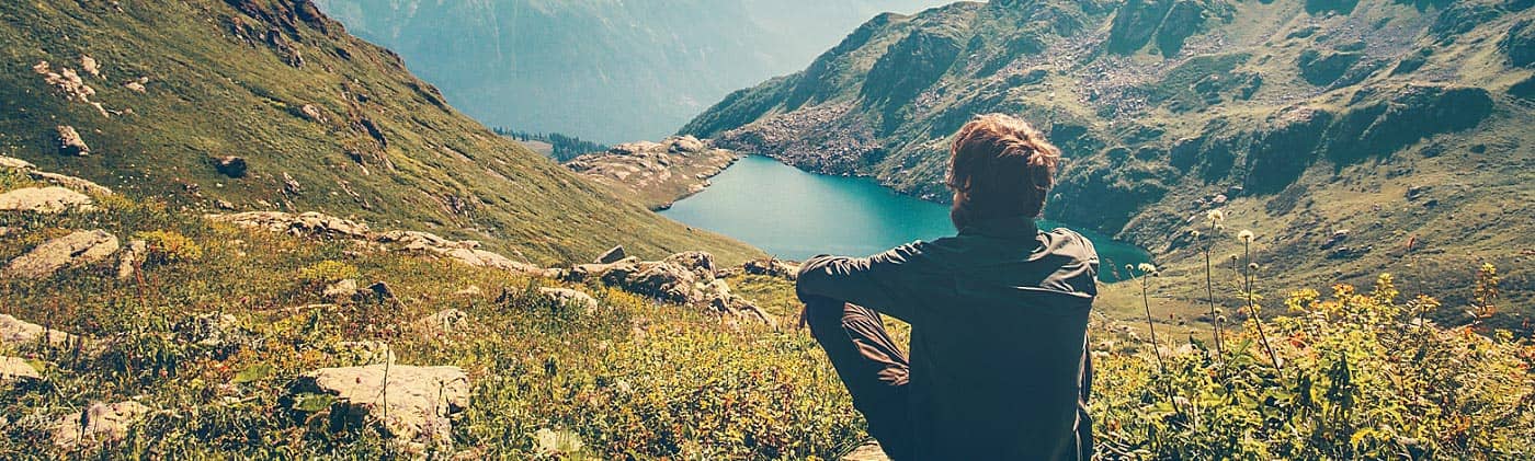 man on hike sits and looks at a beautiful mountain lake as he thinks about personal insurance plans