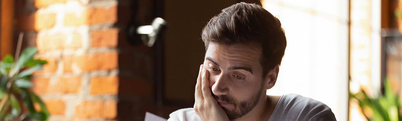 A man sitting in front of his laptops reviews his student loan debt assistance options 