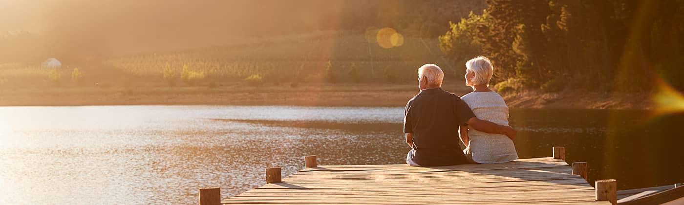A mature couple sits on a dock by a lake and discusses how to invest in retirement 