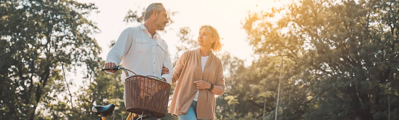 A mature couple walks alongside a bicycle after saving for health care costs in retirement. 