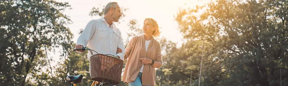 A mature couple walks alongside a bicycle after saving for health care costs in retirement.