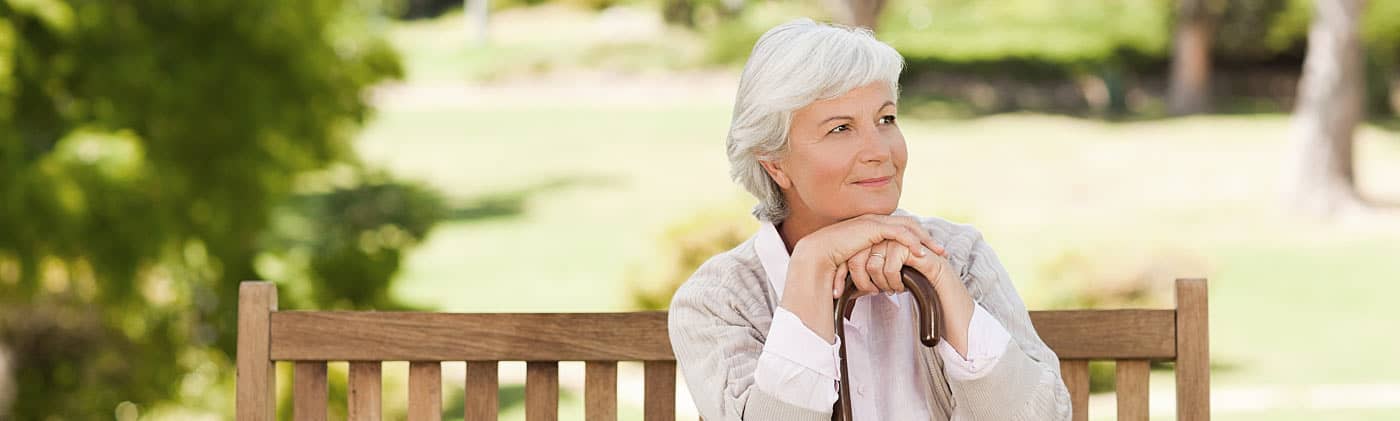 A old woman sitting on a park bench smiling after retiring single