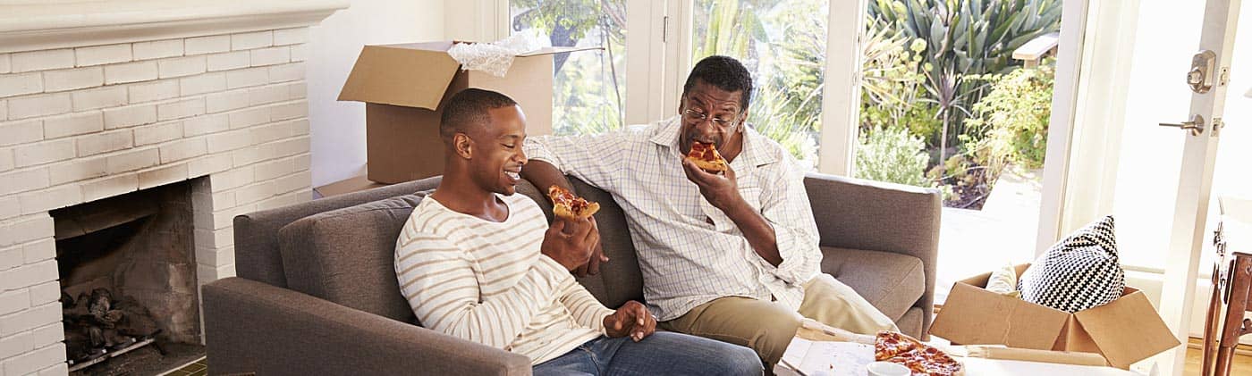 senior father and his adult son eat pizza after hauling boxes to celebrate his moving after retirement