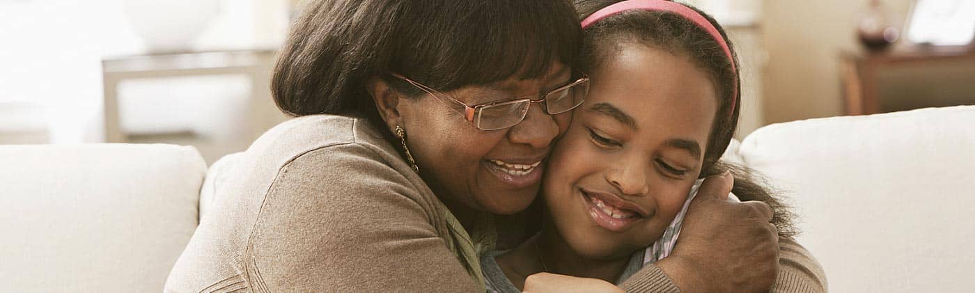 A smiling grandmother hugs her granddaughter in the living room: life insurance for children