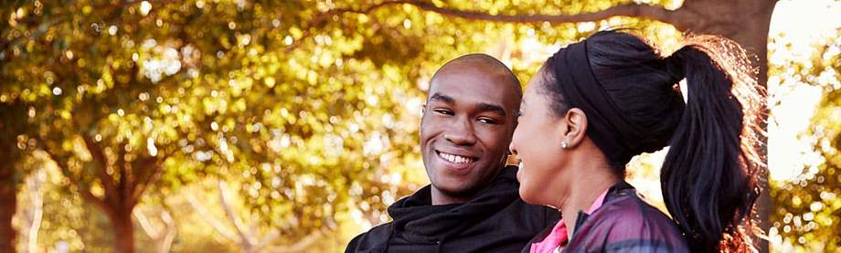 smiling young couple sits on a bench in a park to discuss their new jobs’ pension plan benefits