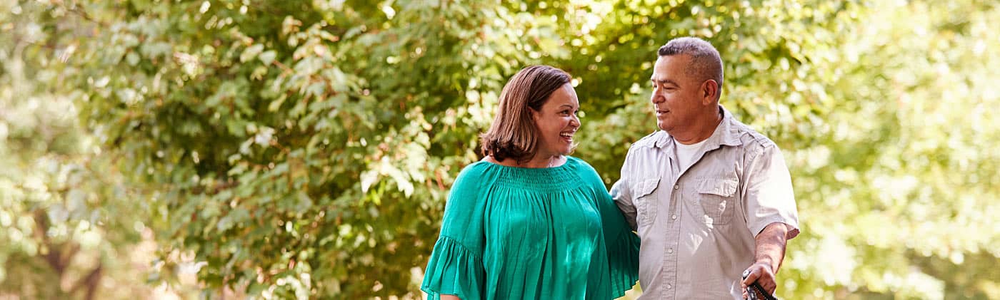 A couple takes their dog for a walk in their neighborhood and discusses how to invest for retirement 