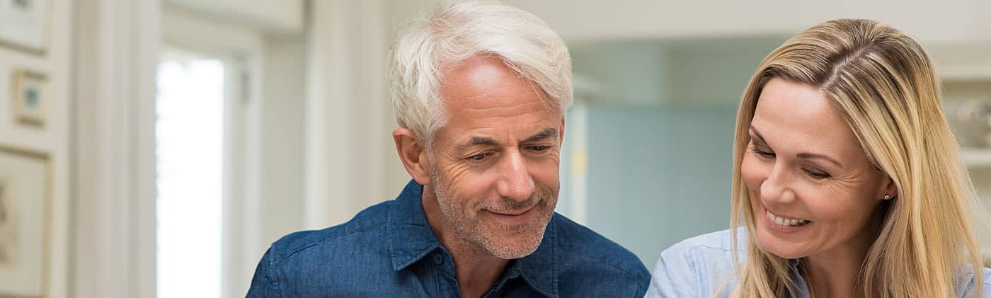 A middle-aged couple sits at a table and looks at papers regarding their retirement income planning 