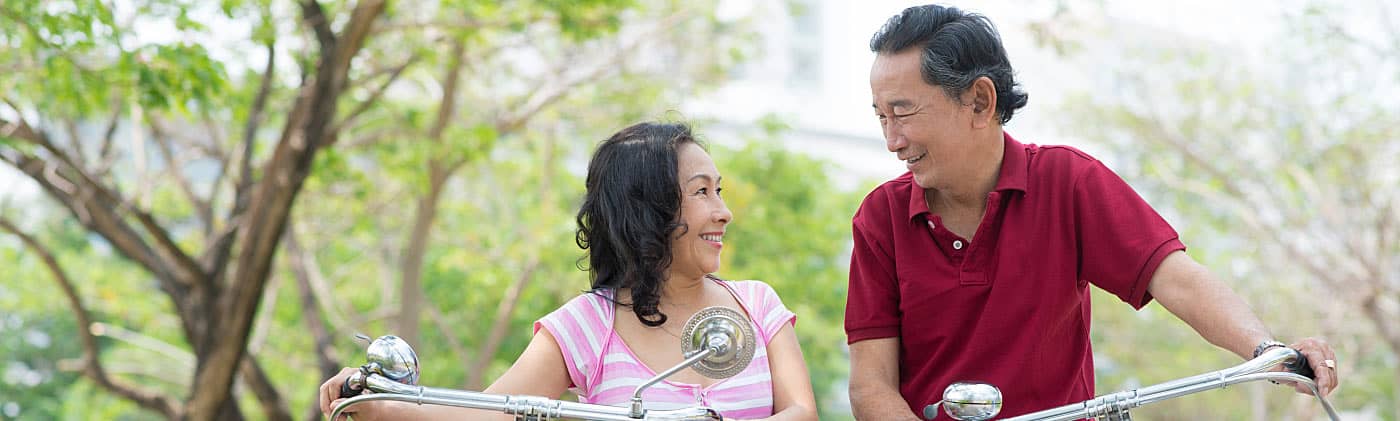 Asian couple riding bikes and discussing 401(k) loan vs. hardship withdrawal 