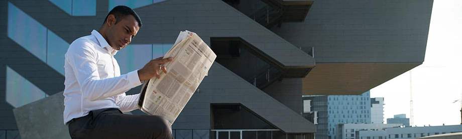 businessman sits outside office and checks performance of mutual funds vs. stocks in newspaper