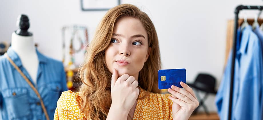 Thoughtful woman holding a credit card in a clothing store, appearing to contemplate a purchase.