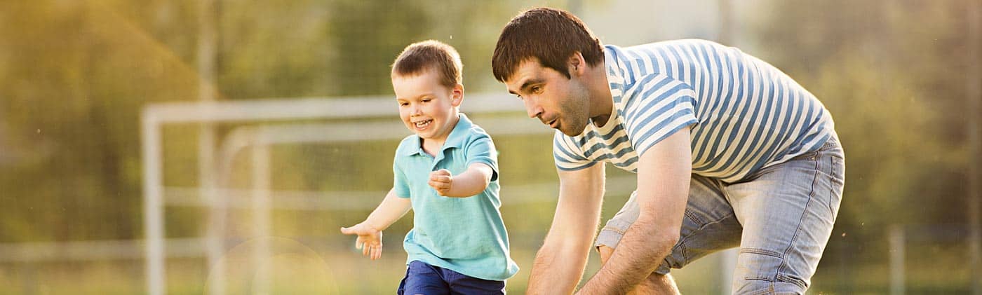 young father with dividend-paying whole life insurance policy plays soccer with his young son