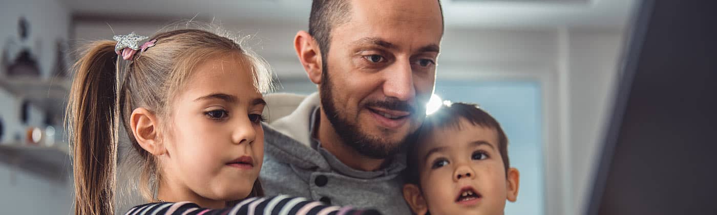 Father sitting with two children in front of computer researching life insurance for single parents