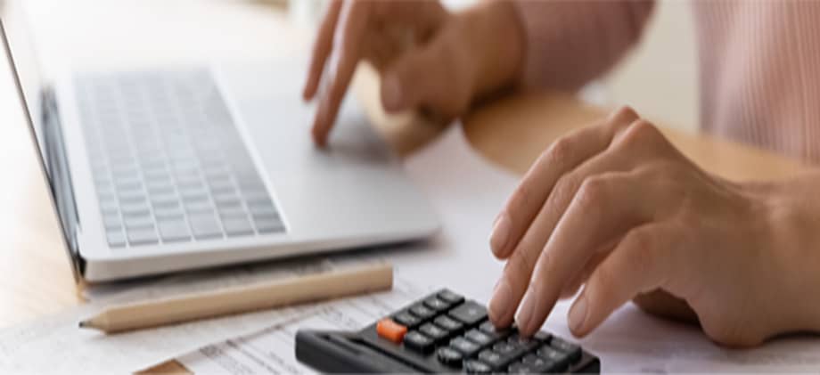 Using a calculator and laptop with financial documents.