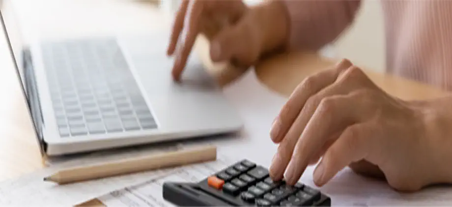 Using a calculator and laptop with financial documents.
