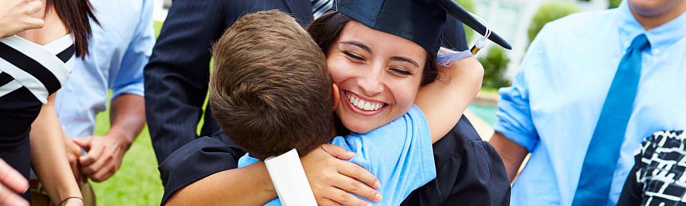 kid brother hugs older sister at college graduation as family is successful in how to save for college