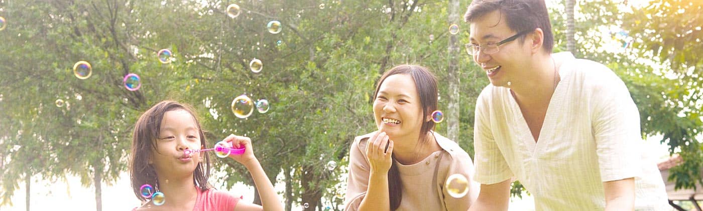 young girl blows bubbles in the park with her parents as they ask themselves do i need life insurance