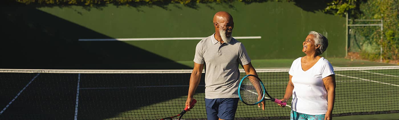 A mature man and woman walking on a tennis court discuss life insurance for people over 50