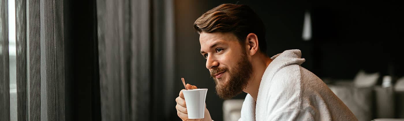 Man drinking coffee in a robe in his hotel room, enjoying a financial windfall during a vacation 