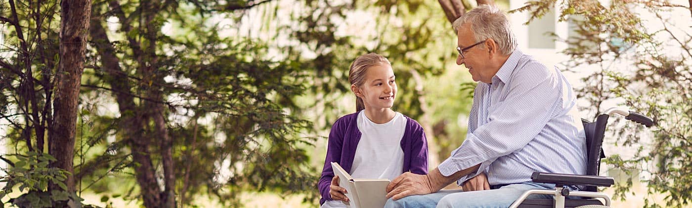 Man in wheelchair reading in the park with granddaughter: long-term care insurance