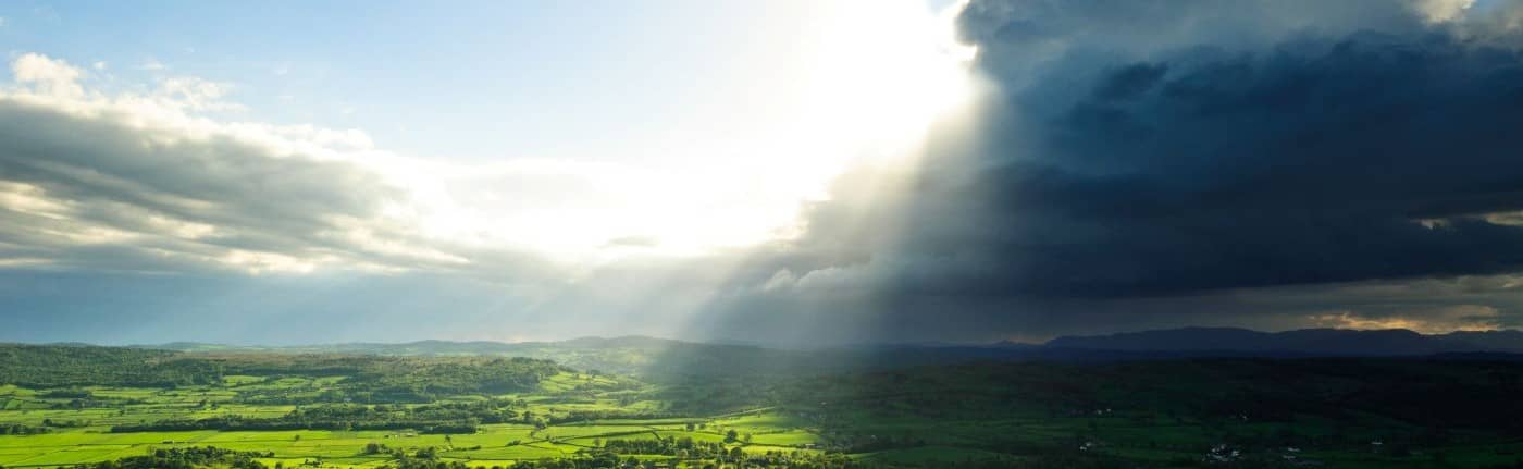 Sun breaking through clouds over landscape.