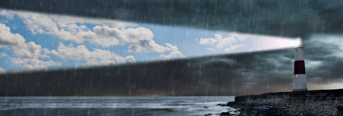 Lighthouse emitting beam of blue sky and clouds in a storm.