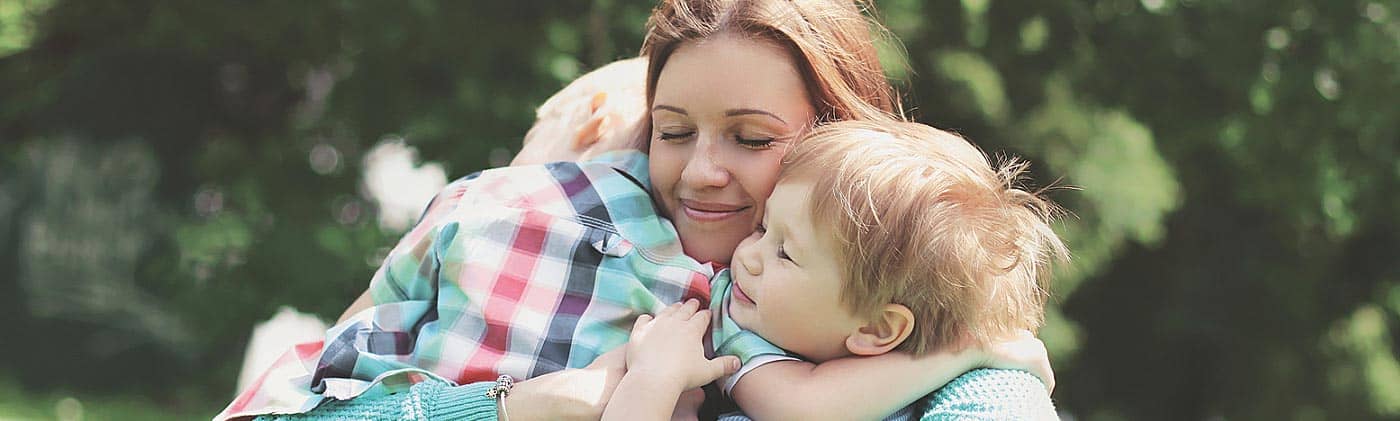 Mother embraces her two young children outdoors: loss of a loved one