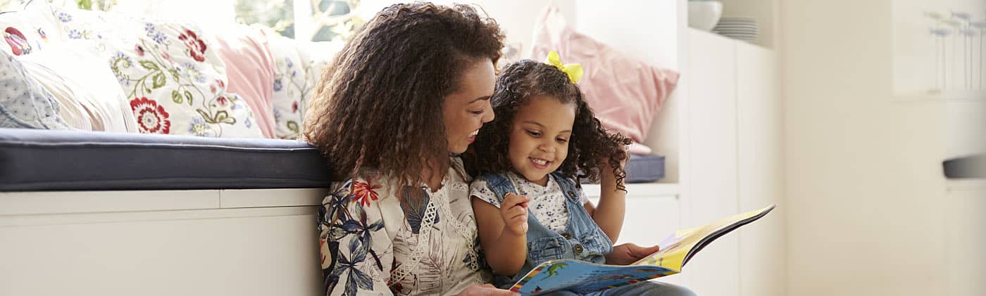 Mother reading with her daughter at home and thinking about how much does it cost to raise a kid 