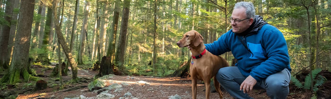Older man walking with dog through woods thinking about finances as a widower