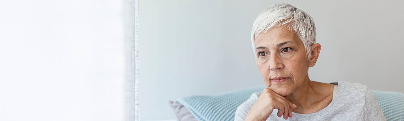 Older pensive woman looking out the window and thinking about running out of money in retirement 