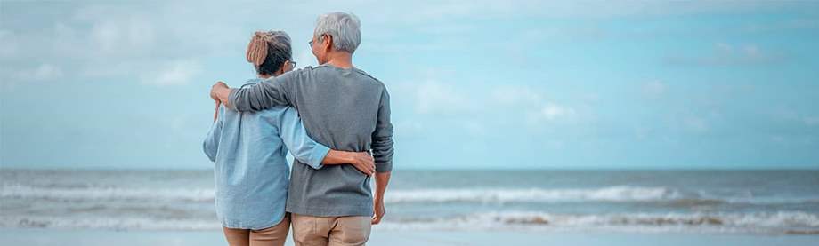 A mature couple walks on a sandy shore as they consider primary vs. contingent beneficiary options 