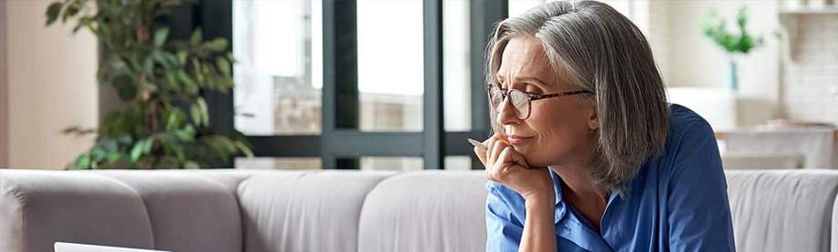A gray-haired woman wearing glasses works on her laptop on the couch wondering what is a SIMPLE IRA? 