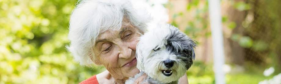 Senior woman holding her dog in a garden while estate planning for pets 