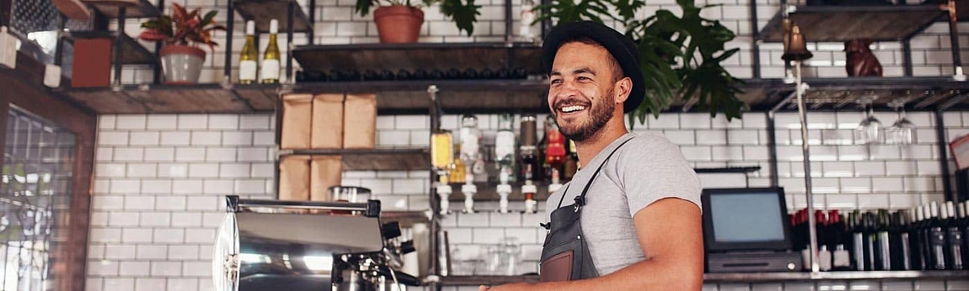 male coffee shop owner smiles inside his cafe and plans to build a quality employee benefits package