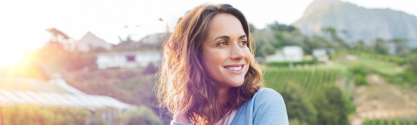 middle-aged woman smiles outside on a farm and wonders: how much do I need to retire at 65?