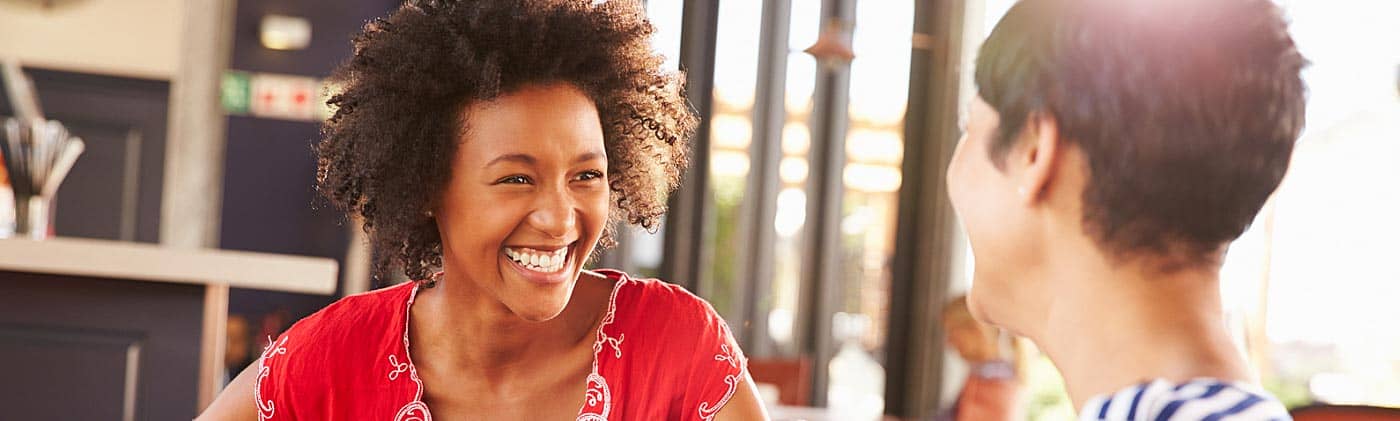 Two 20-something women laugh inside of a well-lit cafe: long-term care insurance