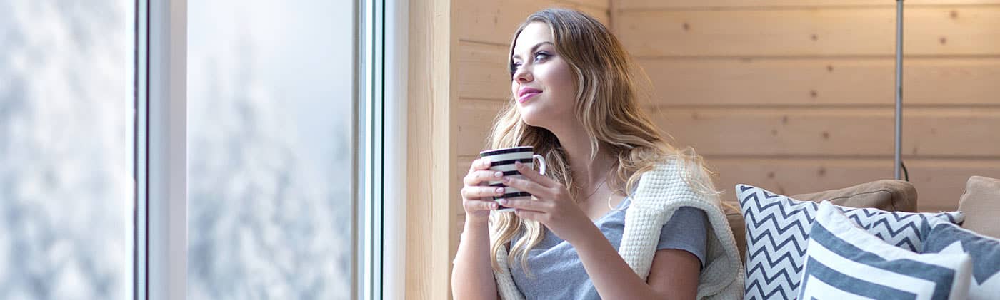 Woman drinking coffee and looking out of her window after conducting a personal finance review