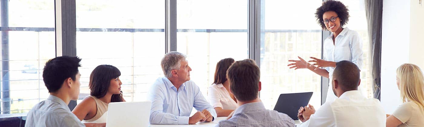 Woman gives a presentation to a group of her peers in a modern office: employer life insurance